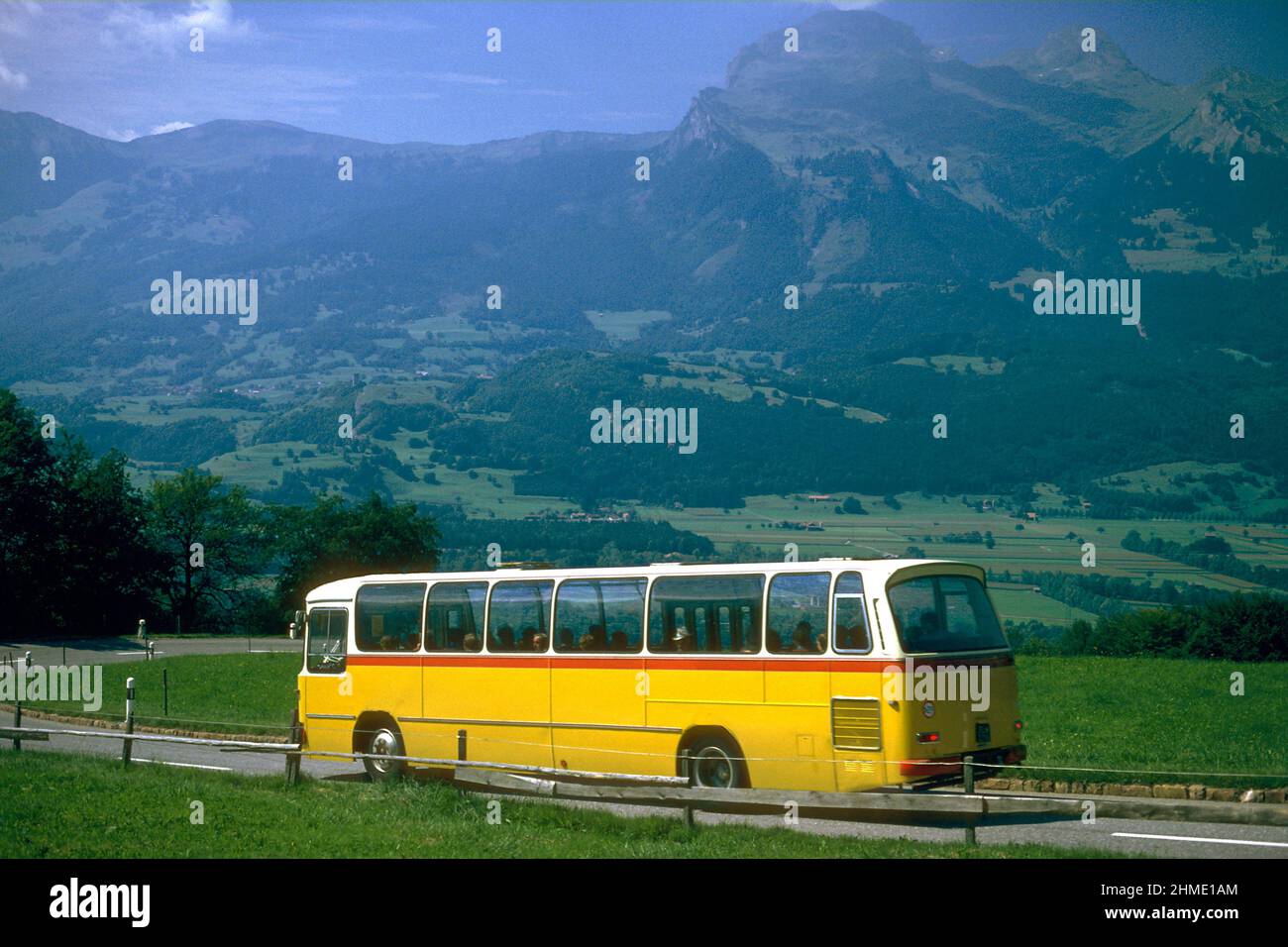Autobús en carretera rural con los Alpes en el fondo en 1981, Triesenberg, Liechtenstein Foto de stock