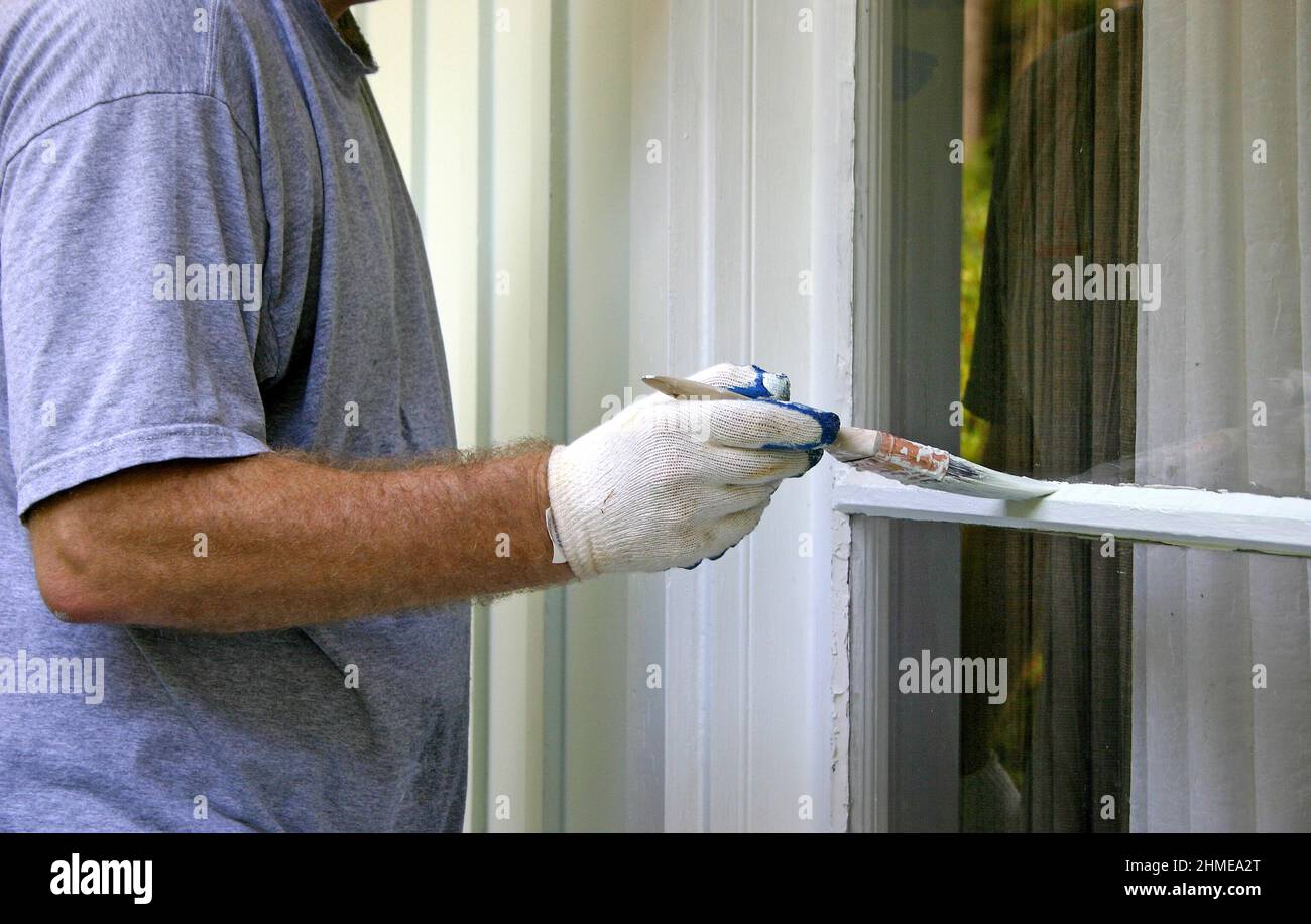 Cerca del brazo de un hombre y mano cuidadosamente pintando el borde de una ventana exterior de la casa Foto de stock