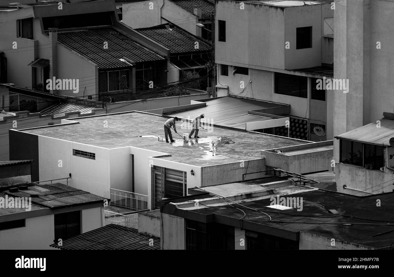 Vida urbana aérea en Quito, Ecuador. Dos hombres en el trabajo, limpiando un techo en blanco y negro. Foto de stock