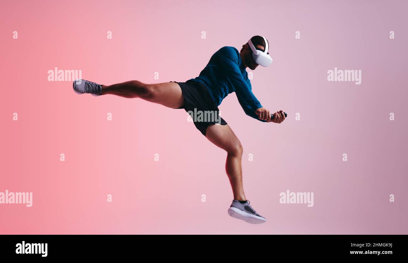 Sportsman saltando al aire mientras lleva puesto un auricular de realidad virtual. Joven atleta experimentando una simulación de 3D. Hombre disfrutando de una formación virtual se Foto de stock
