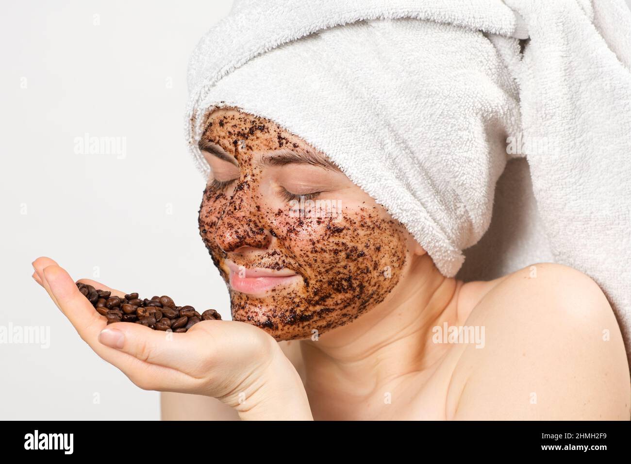 Una mujer con una máscara de café o un exfoliante en su cara sostiene un  puñado de granos de café en su mano Fotografía de stock - Alamy