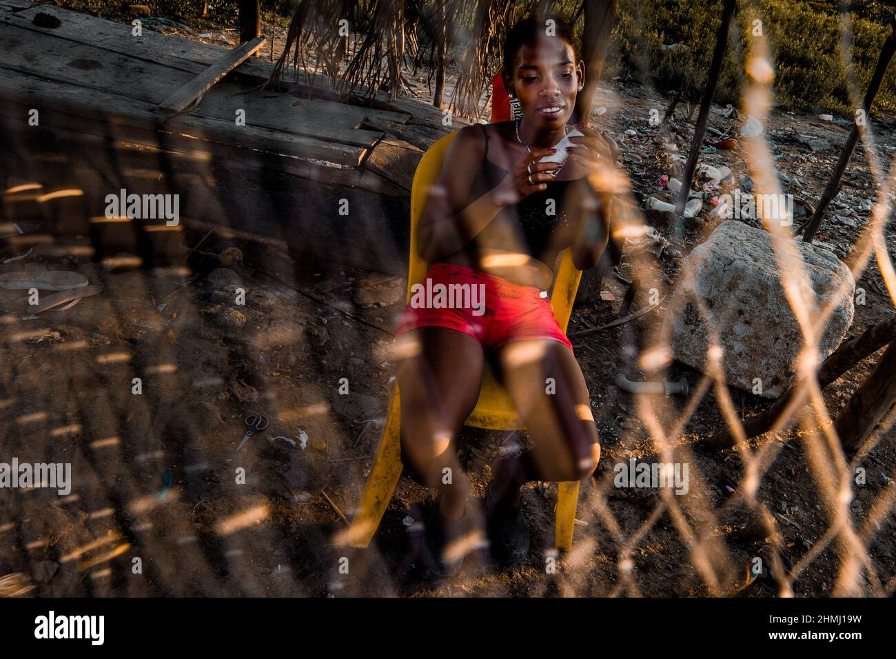Una niña afrocolombiana se sienta detrás de una red de pesca frente a una casa en Olaya Herrera, un barrio de baja clase social en Cartagena, Colombia. Foto de stock