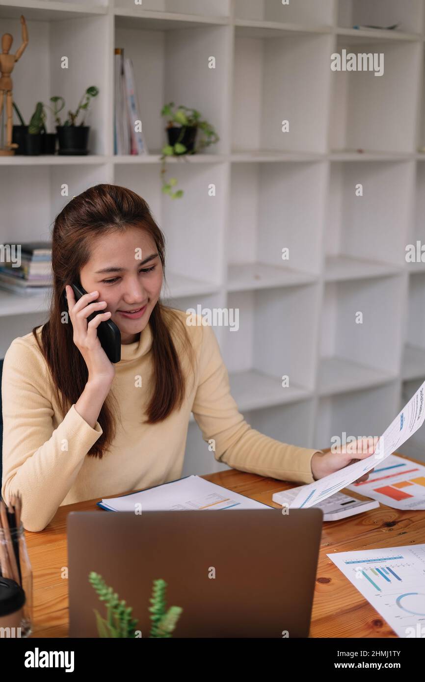 Mujer de negocios asiática haciendo una llamada telefónica, contable trabajando Inversión financiera en calculadora con calcular analizar el negocio y el crecimiento del mercado Foto de stock