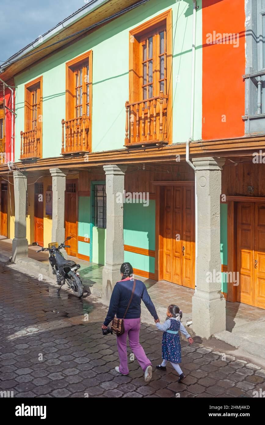 Mujer indígena con niño caminando a la escuela frente a la arquitectura colonial, Quito, Ecuador. Foto de stock