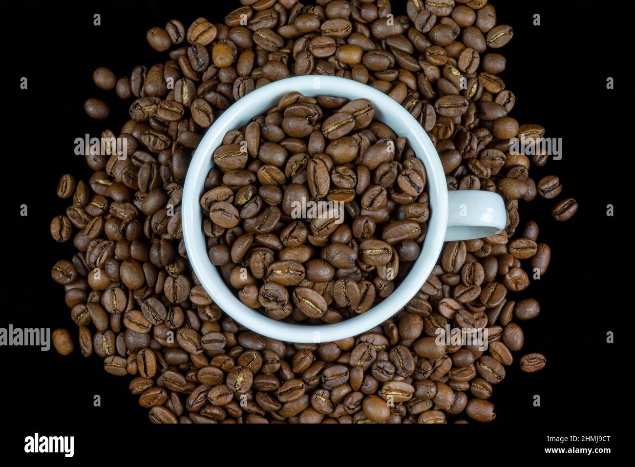 Taza blanca arreglada con granos de café aislados sobre fondo negro Foto de stock