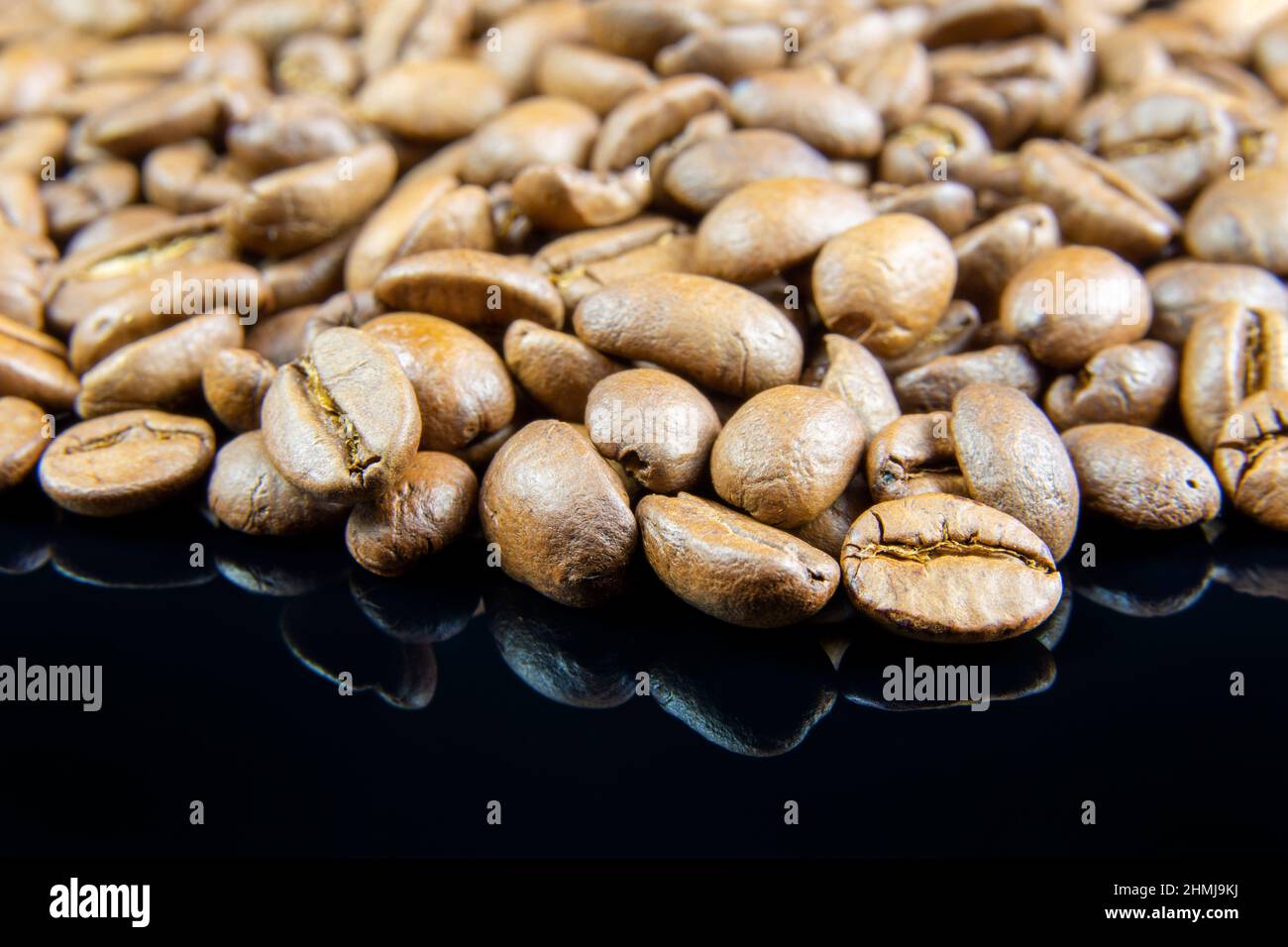 Un primer plano de granos de café sobre fondo negro reflectante Foto de stock