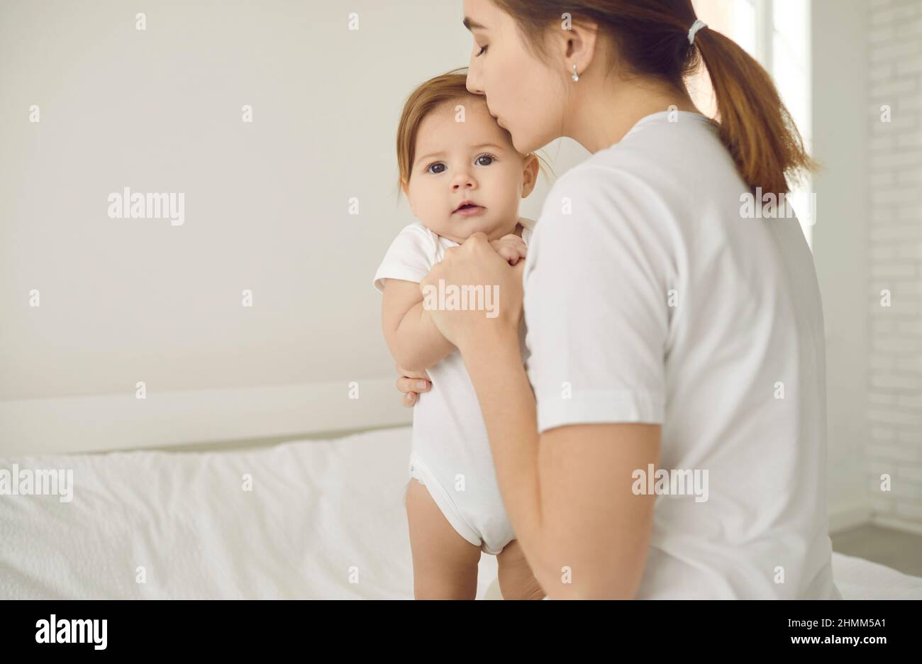 Madre joven besando y calmando a su linda niña que ha sido asustada por algo Foto de stock