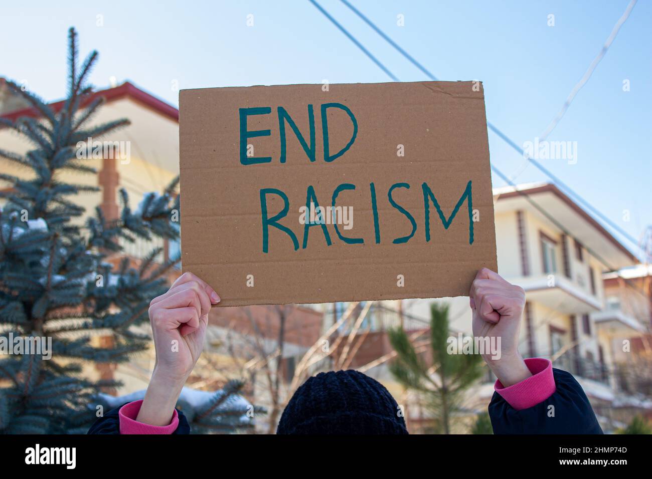 Mano sosteniendo caja de cartón con texto de racismo final. La mujer está protestando contra el racismo. Foto de stock