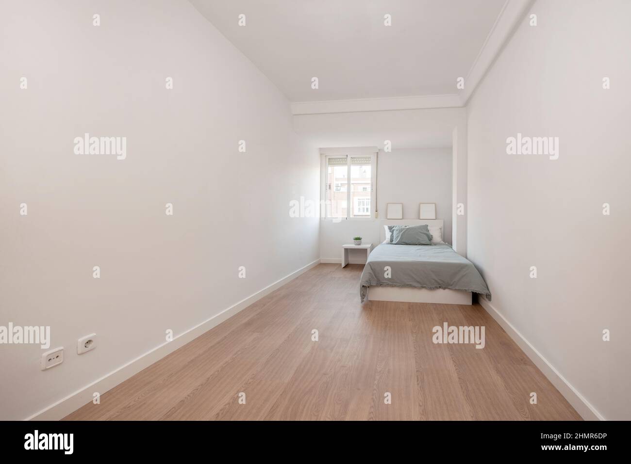 Dormitorio largo con cama junto a la ventana con suelos de madera y paredes  blancas Fotografía de stock - Alamy