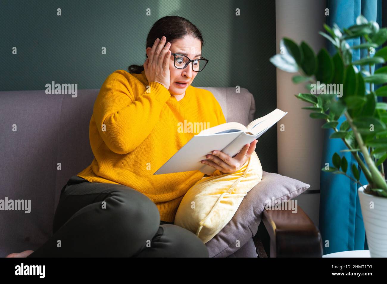 Mujer asustada conmocionada leyendo una novela de terror o un libro de suspense en casa Foto de stock
