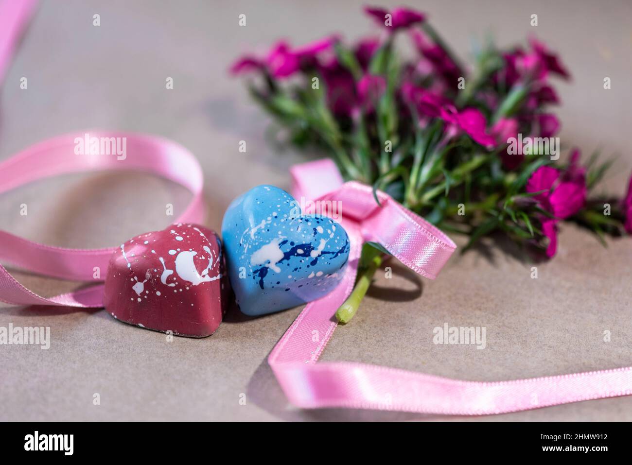 Chocolates en forma de corazón con un montón de flores púrpura en una mesa de madera, cerca, fotografía de la vida fija Foto de stock