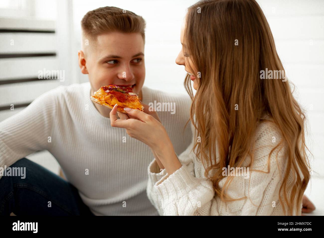 Relación romántica de pareja joven en amor. Hermosa mujer de pelo marrón de pelo largo alimenta a su amigo pizza, que les da gran placer. Concepto Foto de stock