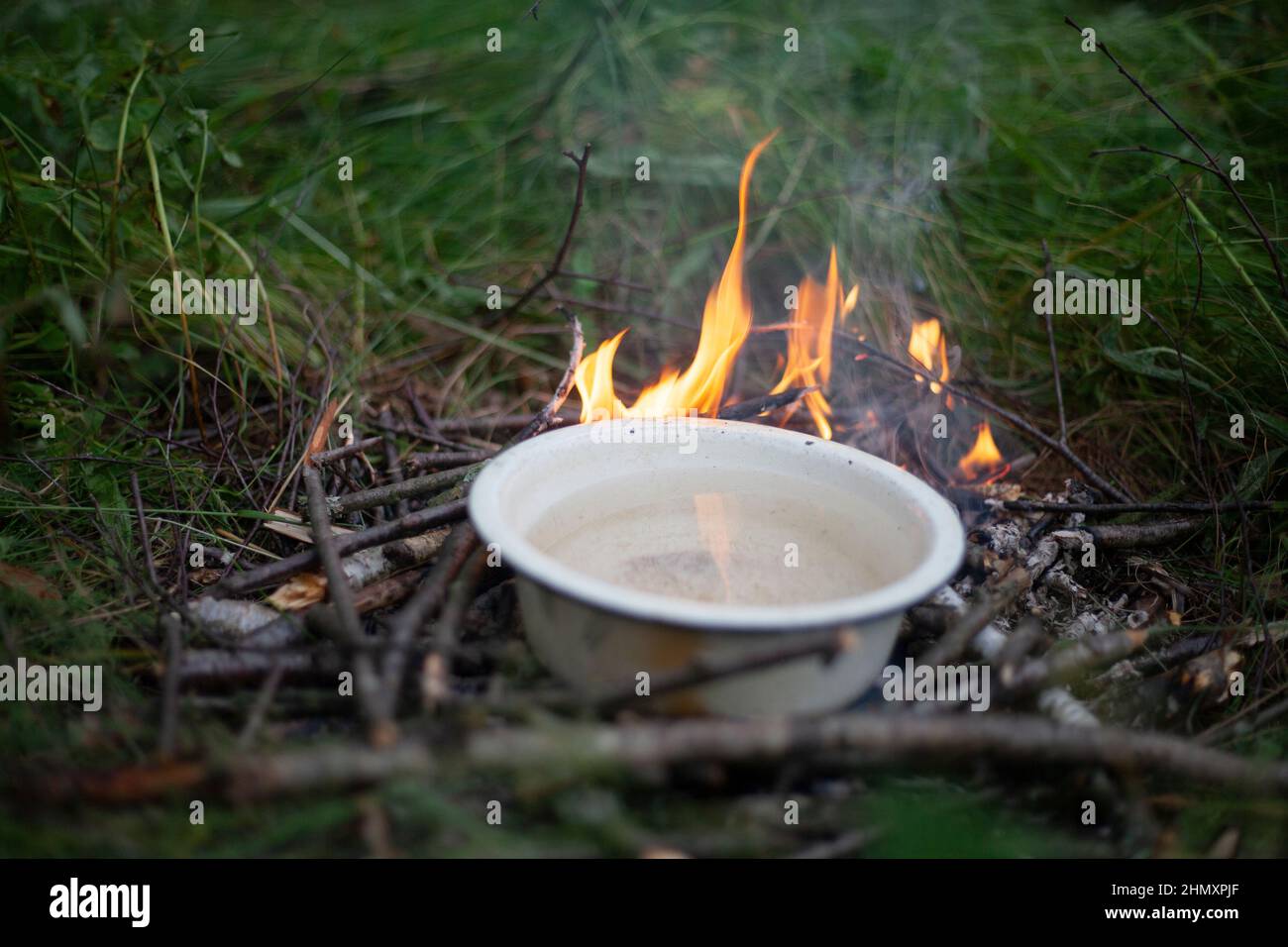 Incendio turístico. Calefacción de agua al fuego. Platos con líquido sobre llama abierta. Cocinar en madera. Agua hirviendo del río en el bosque. Foto de stock