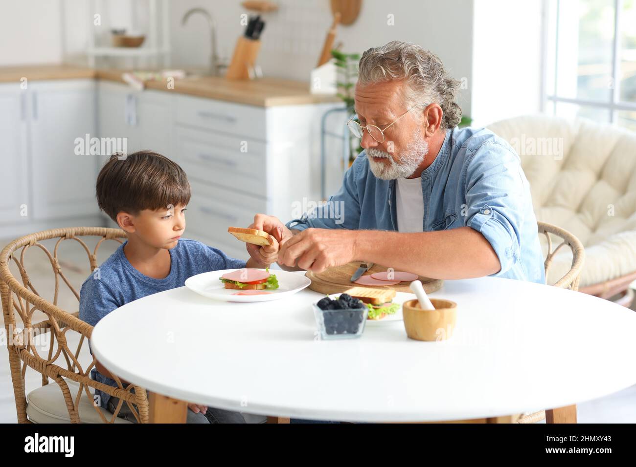 Niño pequeño con su abuelo haciendo un sándwich en la mesa en la cocina Foto de stock