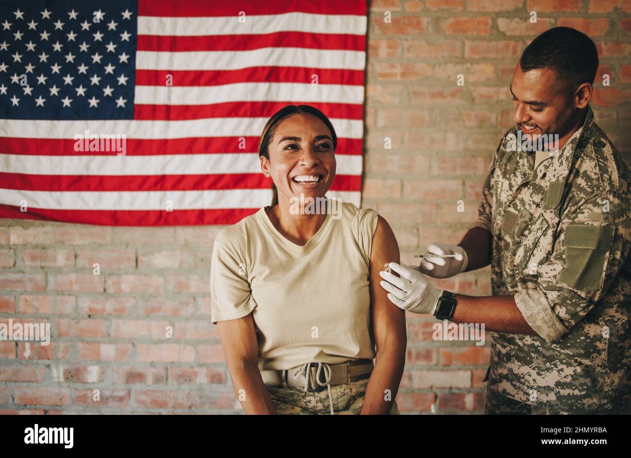 Una mujer militar de los Estados Unidos que recibe una dosis de la vacuna covid-19 en el hospital militar. Alegre mujer soldado sonriendo felizmente mientras se encuentra Foto de stock
