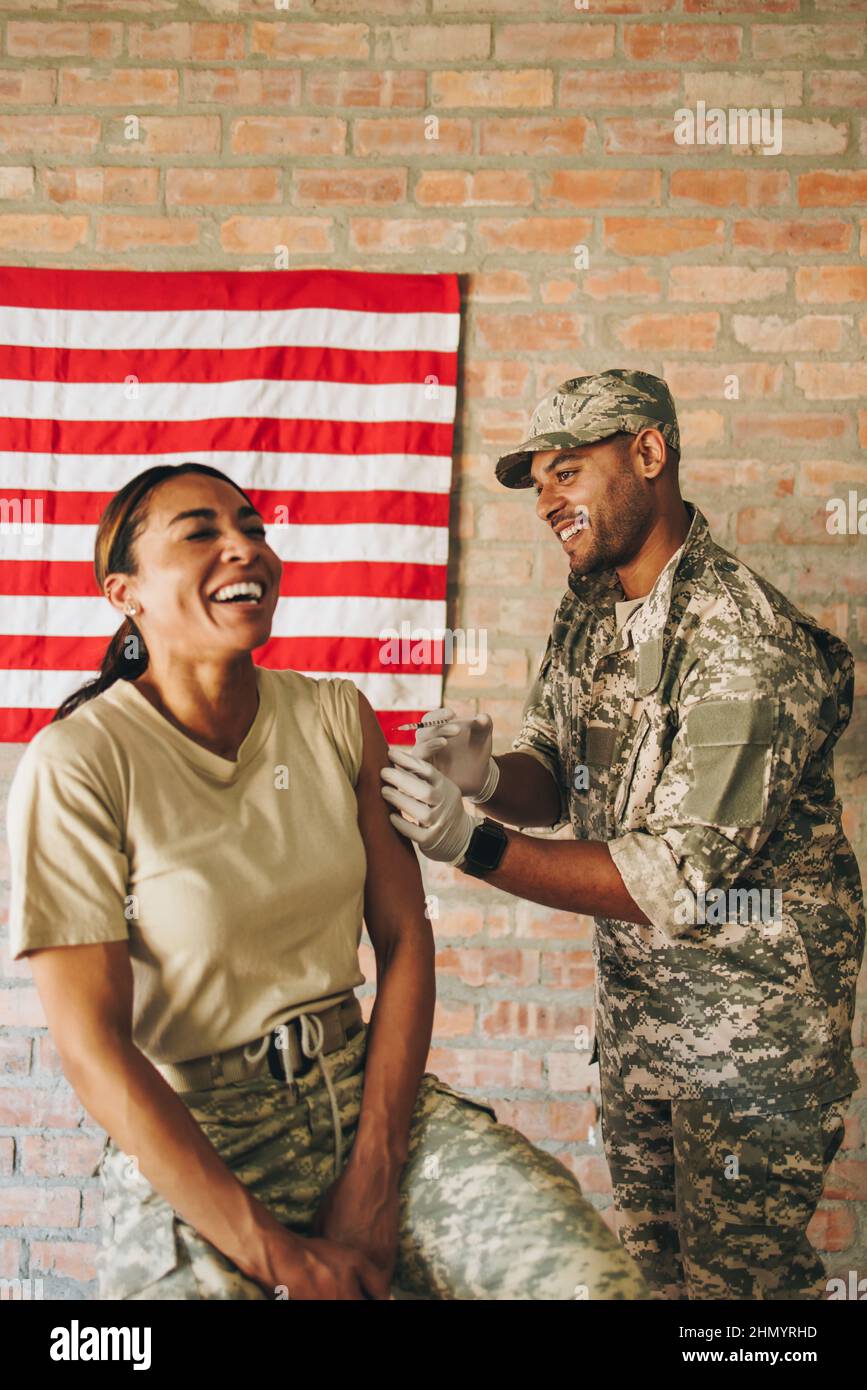 Una enfermera militar feliz inoculando a una soldado durante la pandemia del coronavirus. Médico militar americano inyectando una mujer militar con el covid-19 Foto de stock