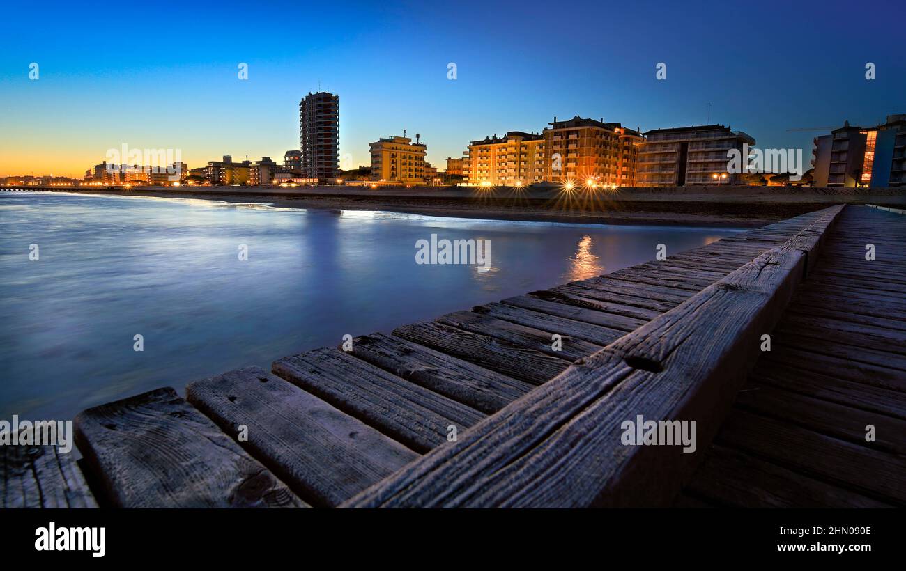 La costa de Jesolo se ve durante la hora azul después de la puesta de sol con el cielo azul y las luces de la ciudad vistas desde el embarcadero de madera en la playa Foto de stock