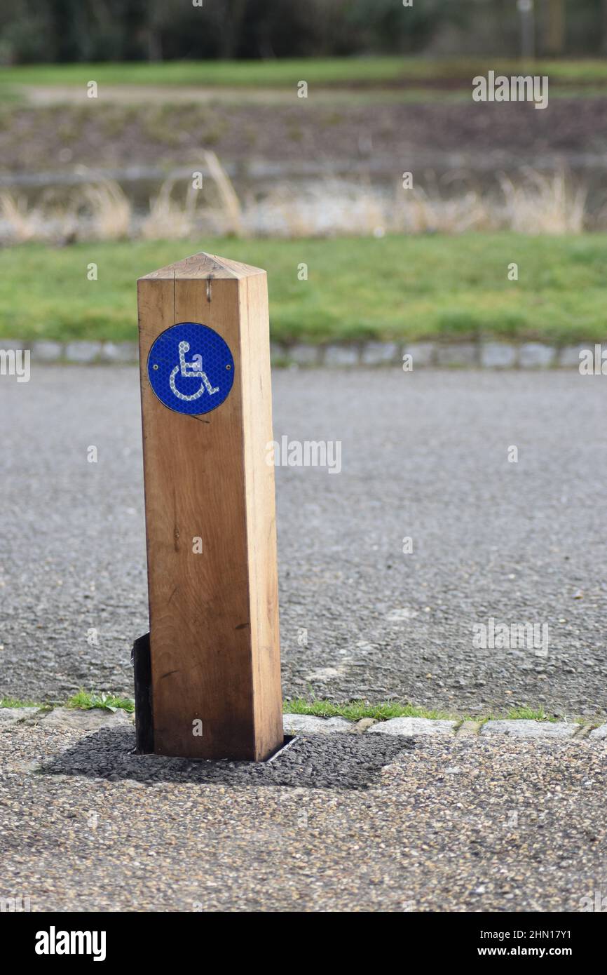 Un poste de madera con un símbolo de discapacidad junto a una plaza de aparcamiento. Foto de stock