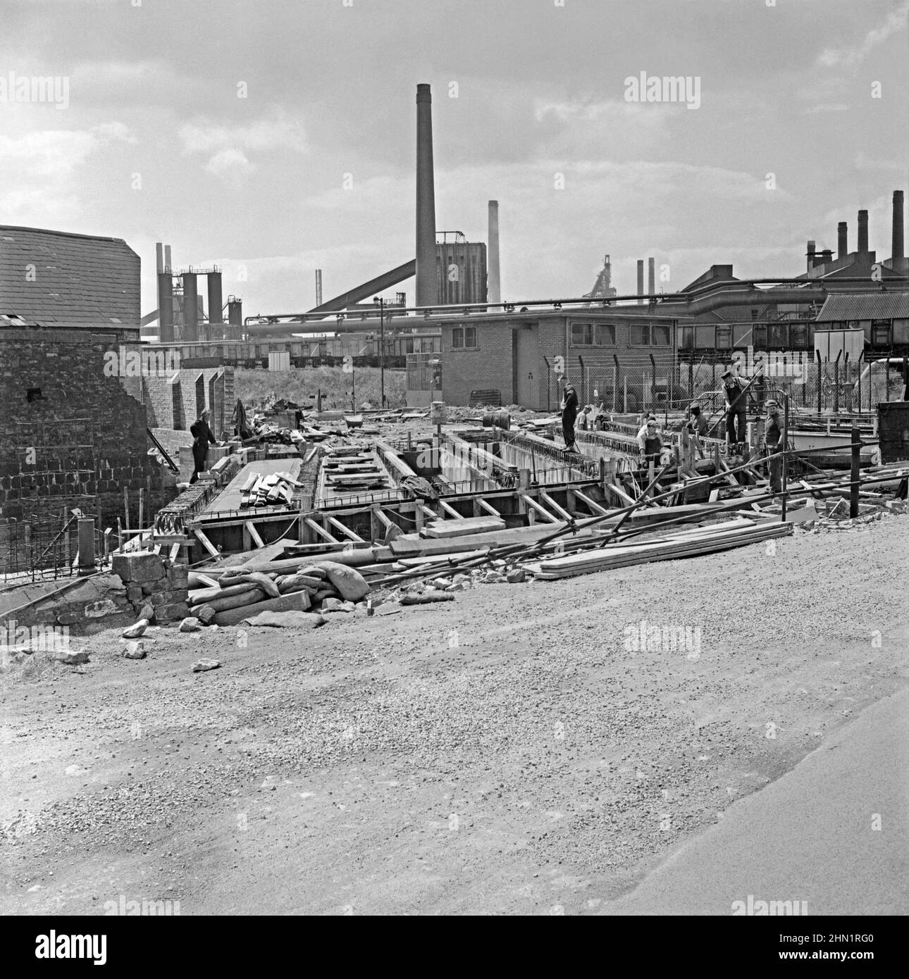 Trabajos de construcción en un nuevo puente sobre el Ffrwd Wyllt en Central Road, Port Talbot, West Glamorgan, Gales, Reino Unido, a finales de los años 1950s. Este iba a convertirse en uno de los principales caminos de acceso a la acería (visto en el fondo) que se había ampliado considerablemente en los años de la posguerra (ver la imagen 2HN1RDT de Alamy para una vista del puente y la carretera terminados). Finalmente, la ruta principal a las obras fue a través de Cefn Gwrgan Road. Sin embargo, ambas vías de acceso fueron cortadas por la construcción de la circunvalación Harbour Way en 2013, una fotografía de la época de 1950s. Foto de stock