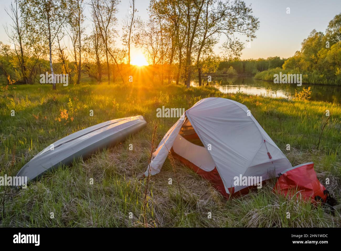 Paisaje con tienda de campaña y kayak en el río al amanecer Foto de stock