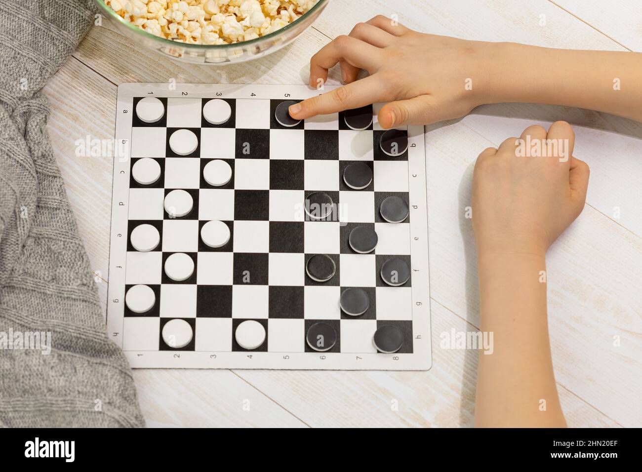 Un juego de damas. Descanso en casa. Un tablero de ajedrez con damas y la  mano de un niño haciendo un movimiento en un piso de madera con manta de  punto y