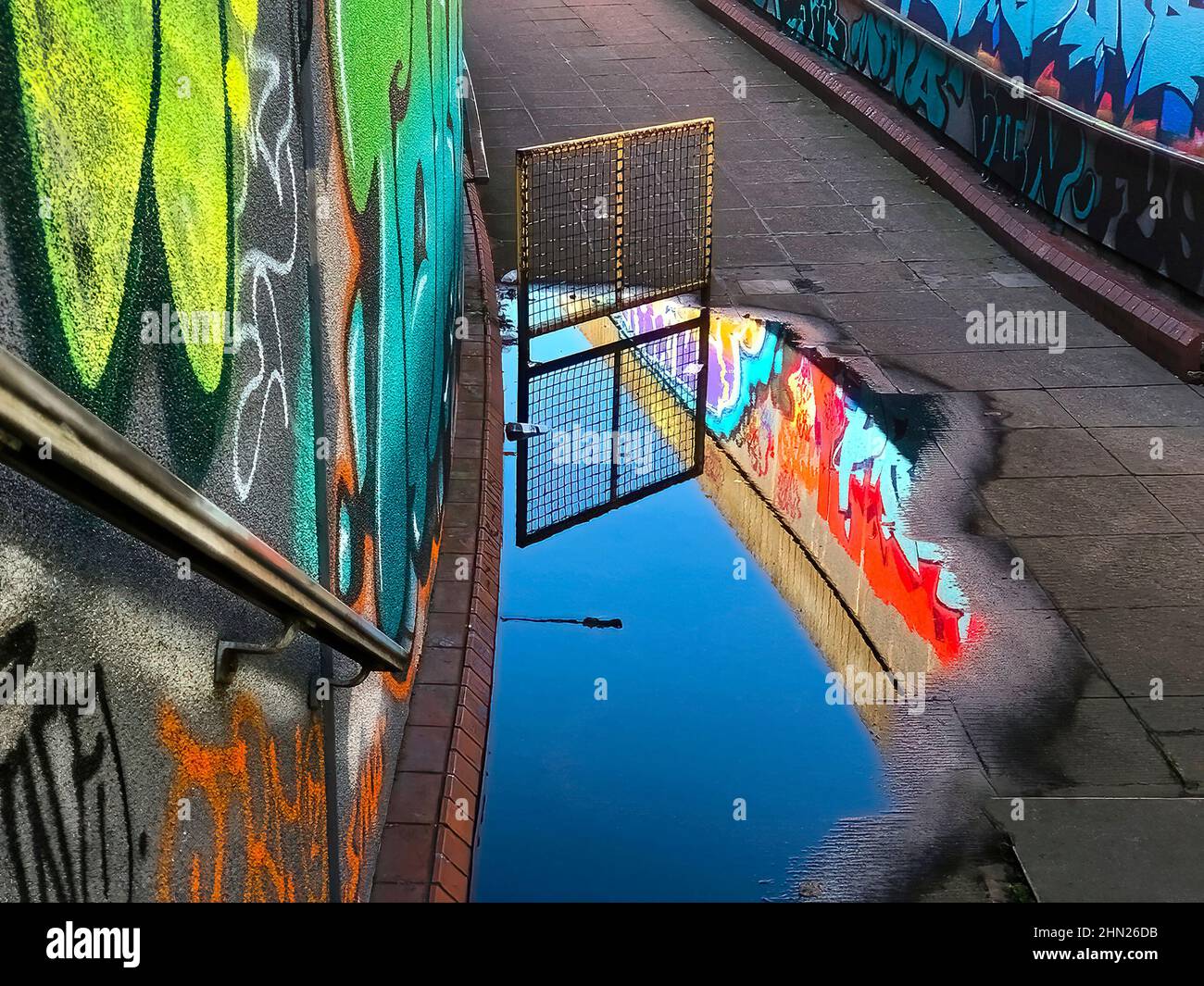 Baje hasta el paso subterráneo bajo una carretera principal en Leicester que refleja las paredes cubiertas de graffiti en el charco de lluvia Foto de stock
