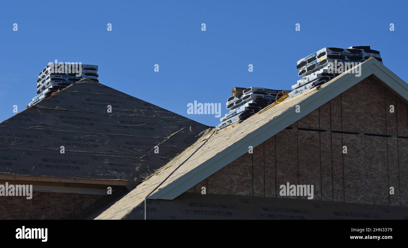 Se apila un montón de tejas en el techo de una casa en construcción en una nueva subdivisión residencial en Langford, British Columbia, Canadá Foto de stock