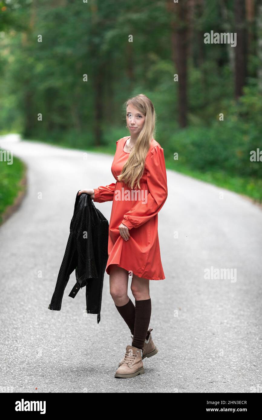 Una chica con un vestido rojo claro y aireado, una chaqueta de cuero en estilo rocoso en una carretera vacía en un bosque de verano Fotografía de stock - Alamy Una chica con un vestido rojo claro y aireado, una chaqueta de cuero en estilo rocoso en una carretera vacía en un bosque de verano Fotografía de stock - Alamy
