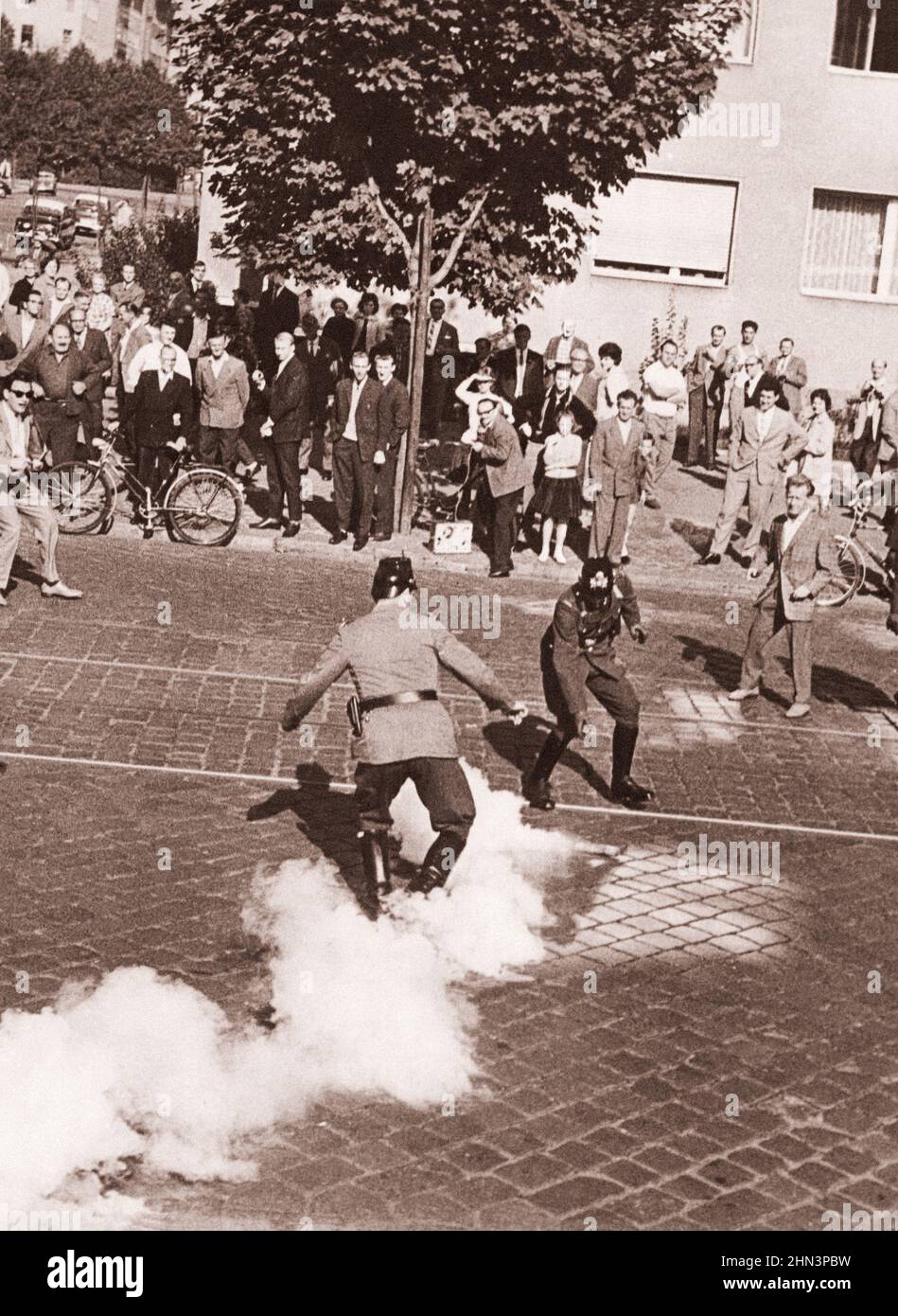 Foto vintage de la crisis de Berlín de 1961: Construyendo el Muro. Juego sombrío a través de la barrera. Dos policías del oeste de Berlín se crampan por la granada mientras golpea a Gro Foto de stock