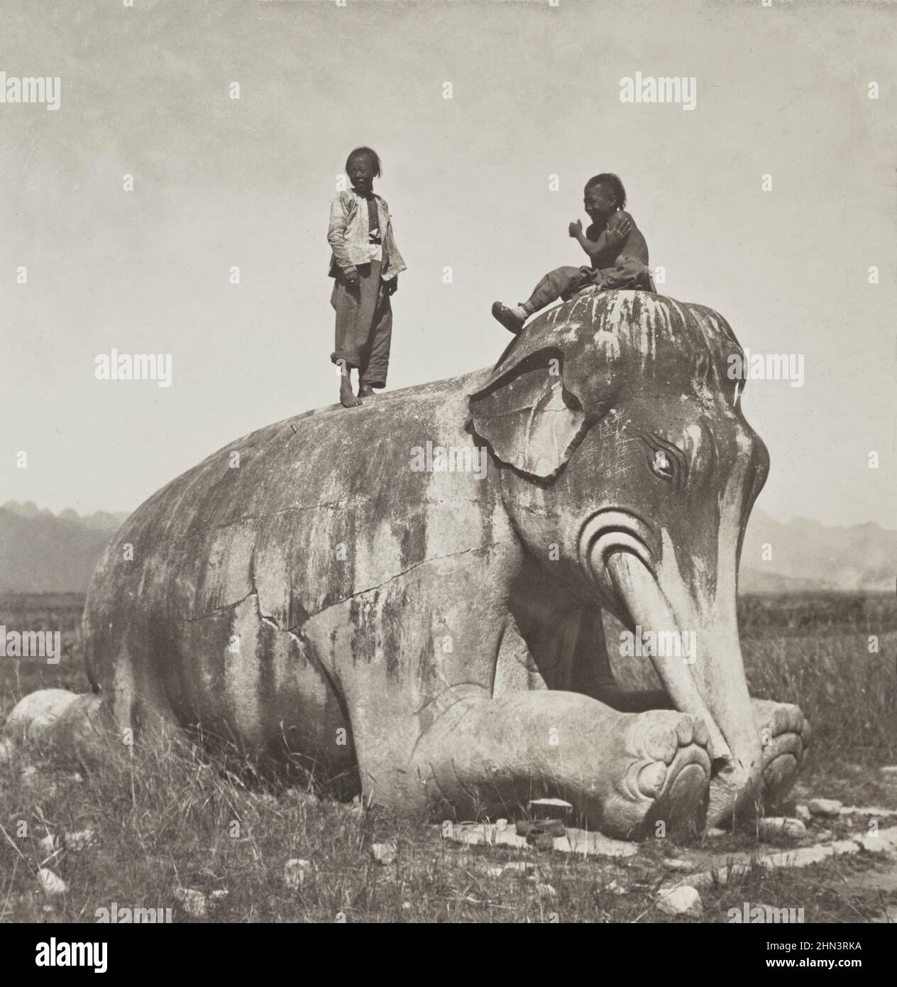Foto vintage de niños chinos con cola en la parte superior de las estatuas de elefantes arrodillados en la avenida de los animales de piedra, las tumbas Ming. Norte de China. Julio de 190 Foto de stock