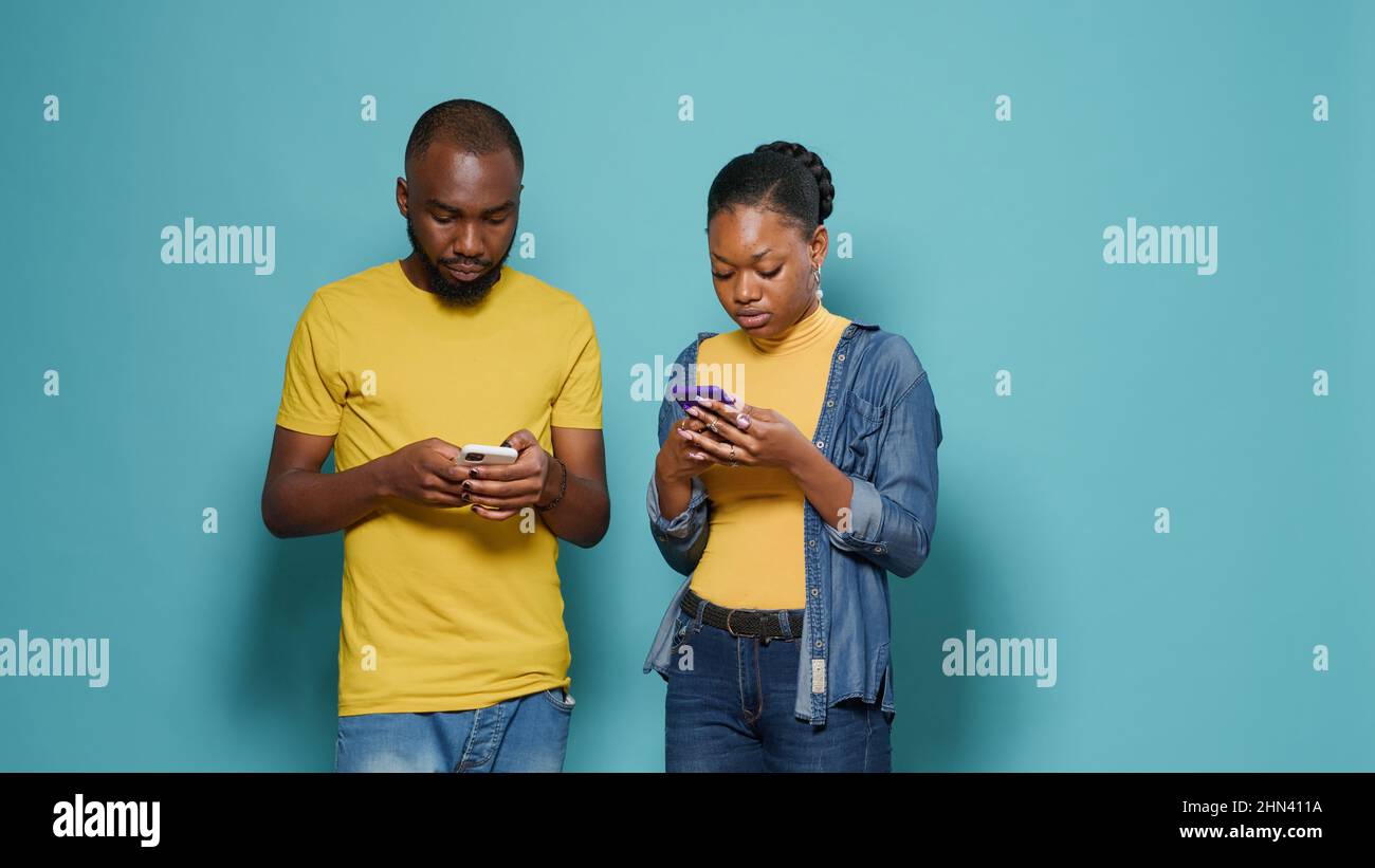 Pareja afroamericana que utiliza smartphone para enviar mensajes de texto  en el estudio. Hombre y mujer modernos mirando la pantalla del teléfono  móvil con tecnología. Gente que disfruta de actividades divertidas en