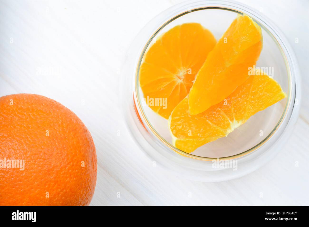 Rodajas de naranja y naranja jugosas enteras en un recipiente transparente junto a él Foto de stock