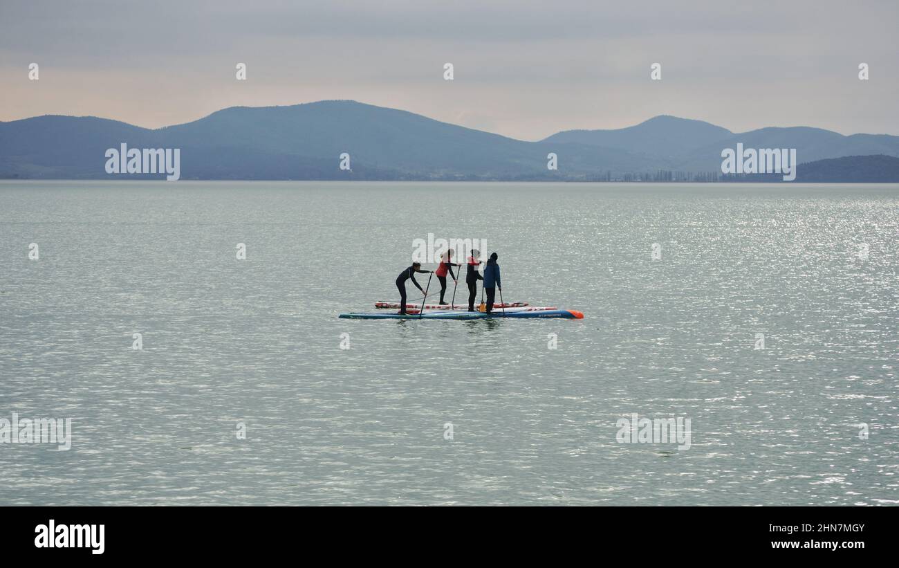 Póngase en pie con un grupo de remo en el flotador de agua en el lago Trasimeno un día frío de invierno Foto de stock