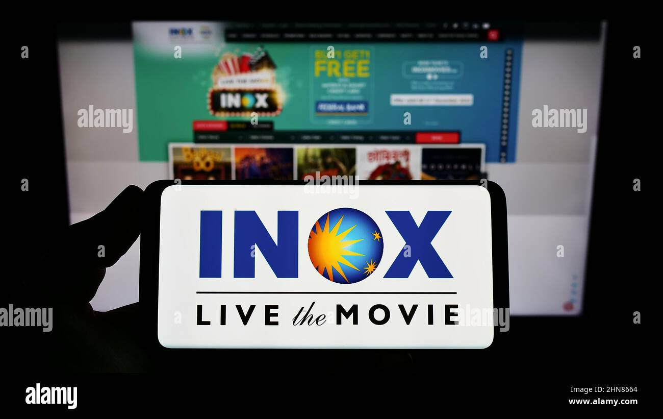 Persona que sostiene un smartphone con el logotipo de la compañía de cine india INOX Leisure Limited en la pantalla delante del sitio web. Enfoque en la pantalla del teléfono. Foto de stock