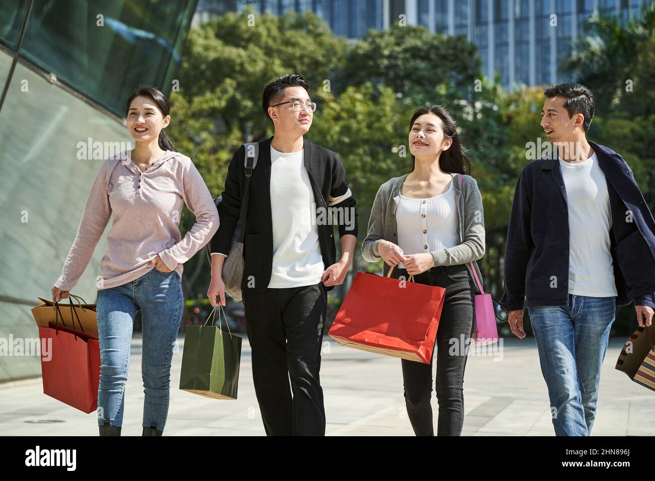 vista de gran angular del grupo de cuatro jóvenes asiáticos charlando conversando mientras caminan por la calle con bolsas de compras en las manos Foto de stock
