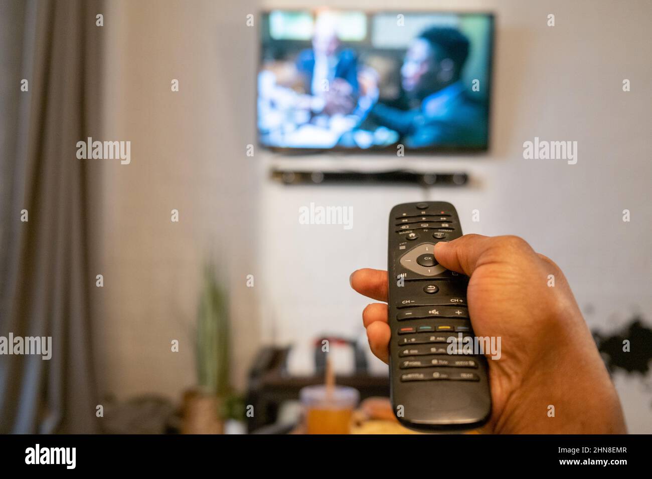 Primer plano de MAN pulsando los botones del mando a distancia para cambiar el canal del televisor de la habitación Foto de stock
