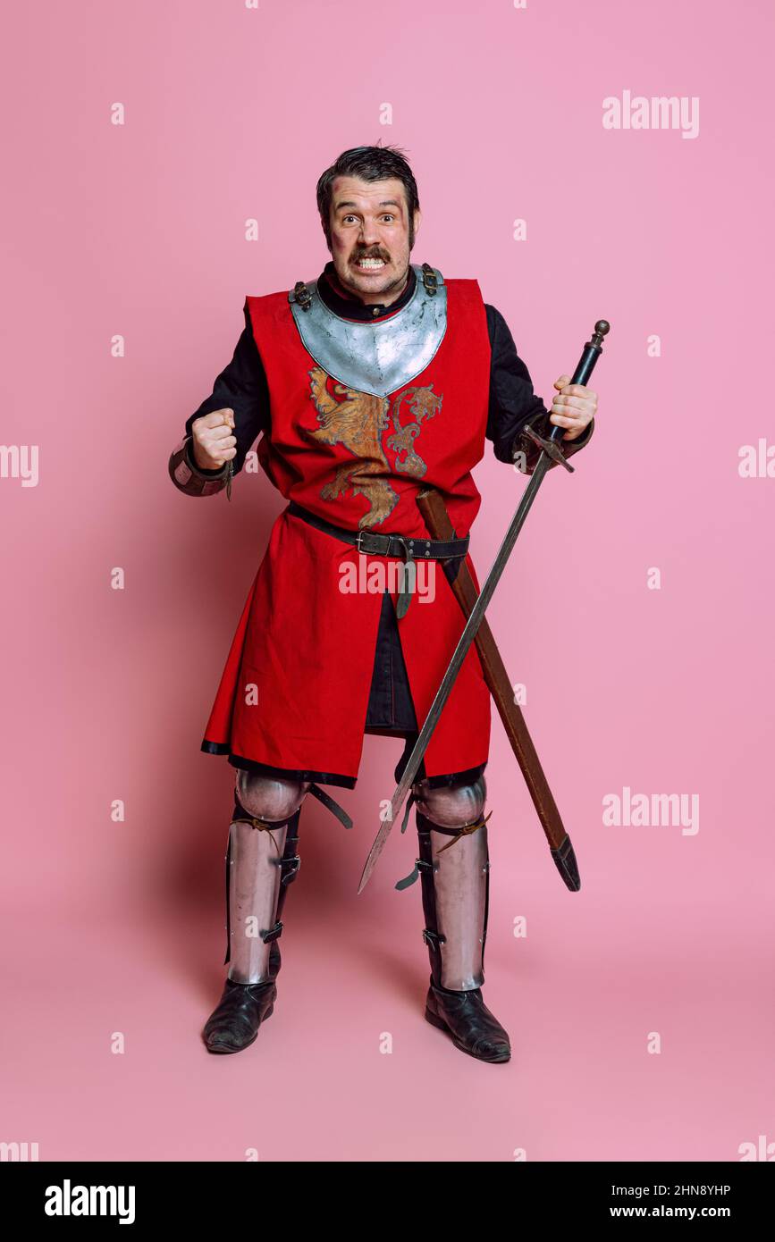 Un hombre joven, guerrero o caballero vistiendo ropa de armadura que se posan sobre fondo rosa. Comparación de eras, historia, emociones Fotografía stock - Alamy