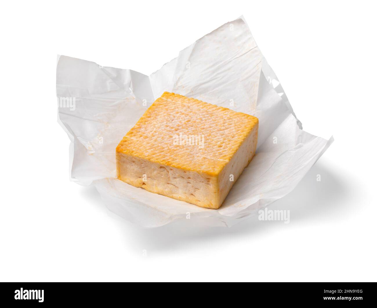 Una sola pieza entera de queso Limburger o Herve con un fuerte olor en papel de embalaje aislado sobre fondo blanco Foto de stock