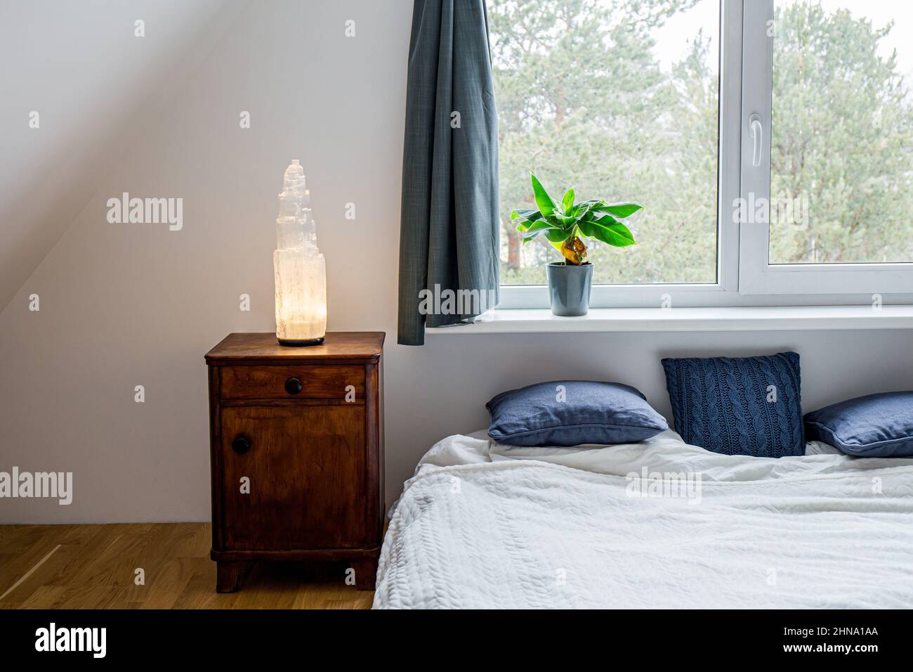 Gran lámpara de poste de torre de cristal selenita iluminada en una mesita de noche de madera en el dormitorio de la casa, decoración espiritual del hogar y luz ambiental. Foto de stock