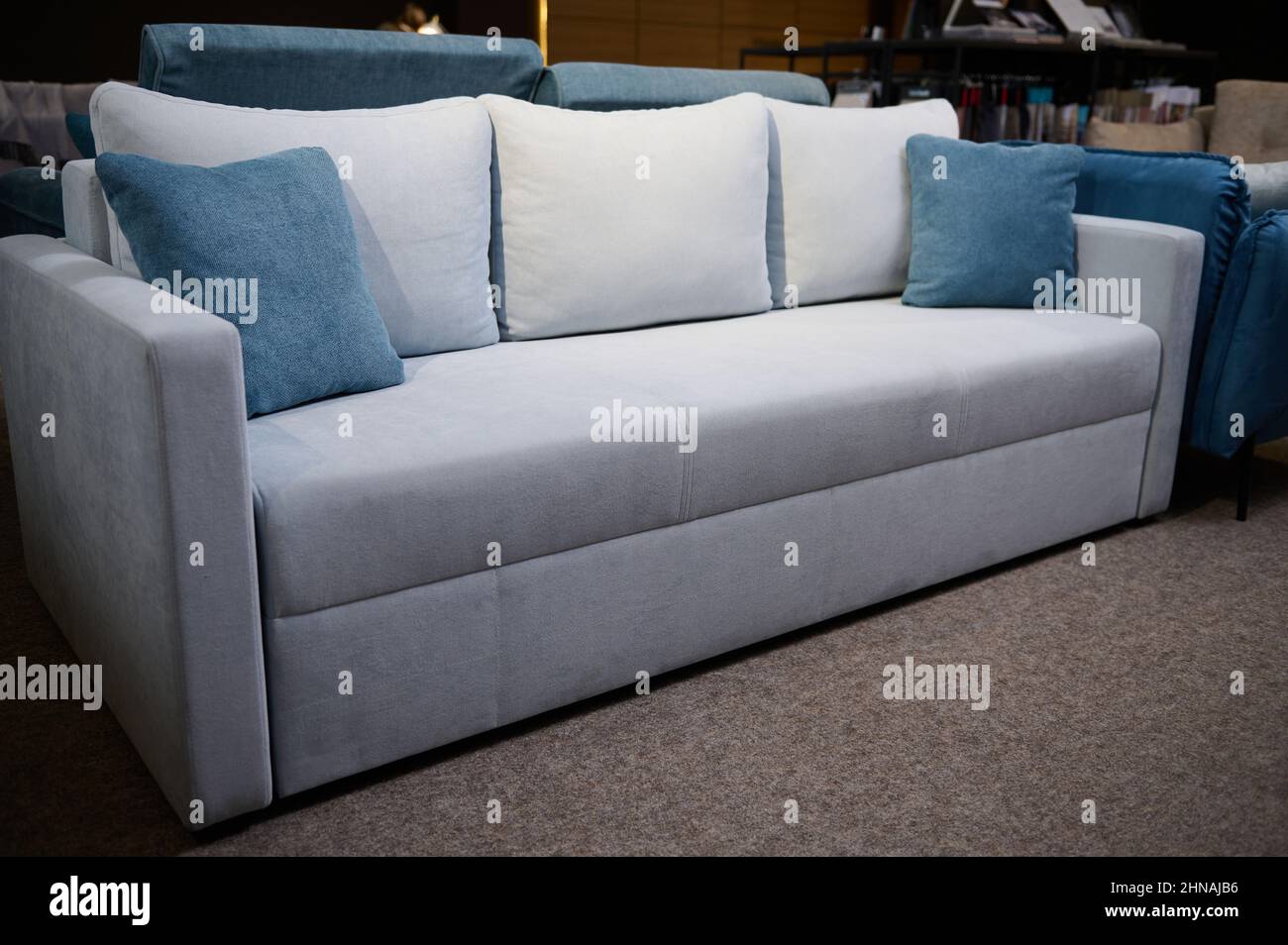 Elegante y minimalista, con sofás de color gris claro y cojines azules, a  la venta en la sala de exposición de la tienda de muebles. Sala de estar  con muebles de estilo