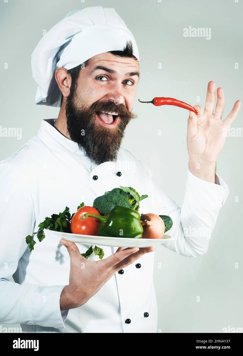 Chef en uniforme con chile y plato con verduras en las manos. Alimentación verde. Alimentos orgánicos Foto de stock