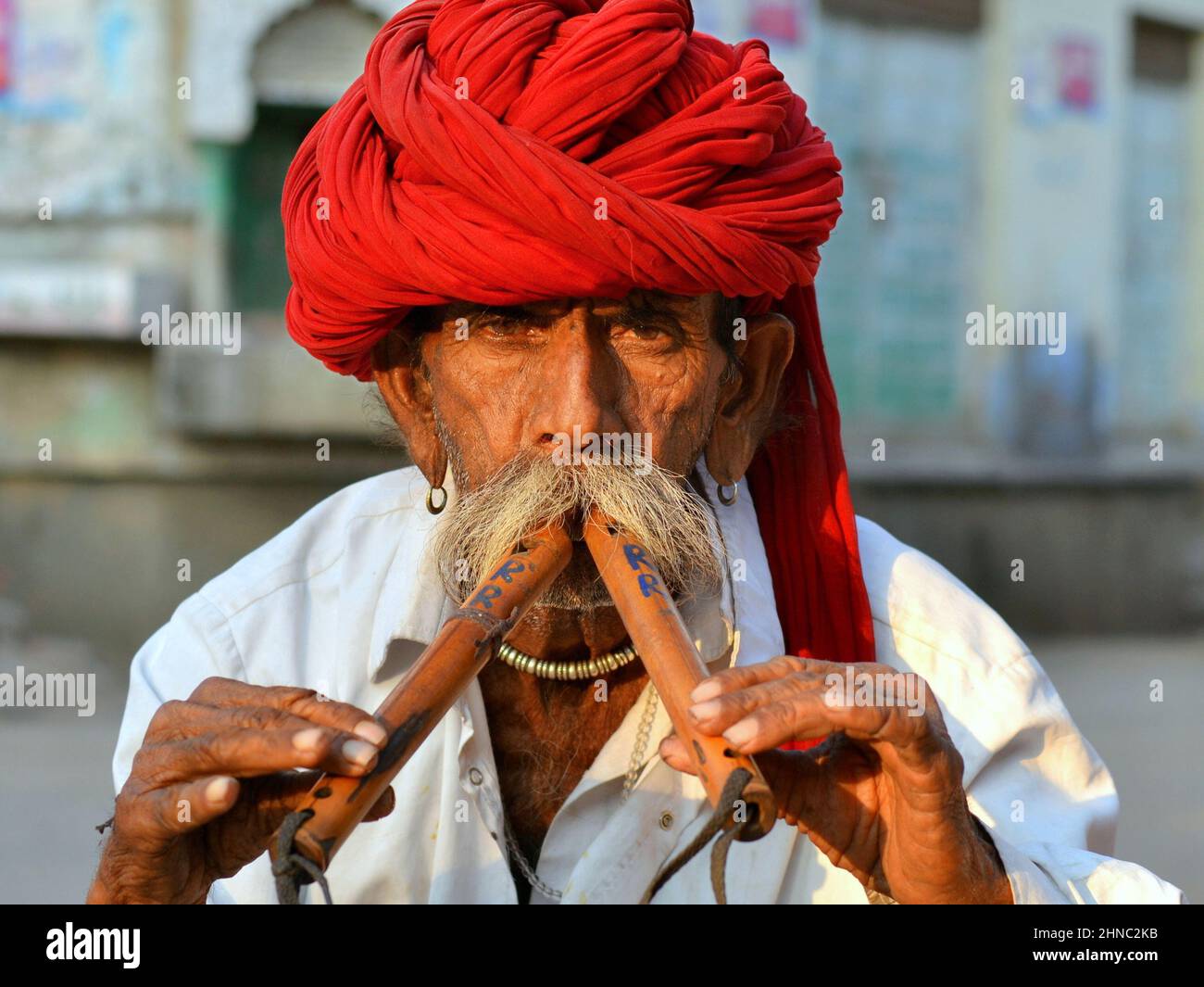 El anciano jugador de flauta doble de alghoza indio lleva un turbante rojo Rajasthani (pagari) y toca sus instrumentos tradicionales de viento de madera con dos manos. Foto de stock