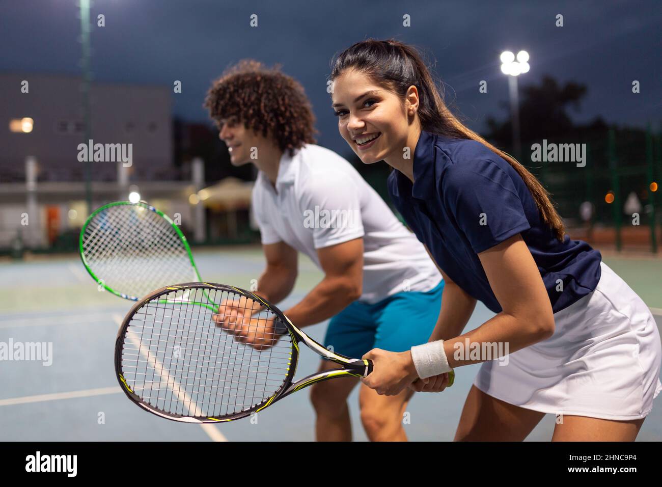 Pareja joven en pista de tenis. Hombre guapo y mujer atractiva están jugando al tenis. Foto de stock