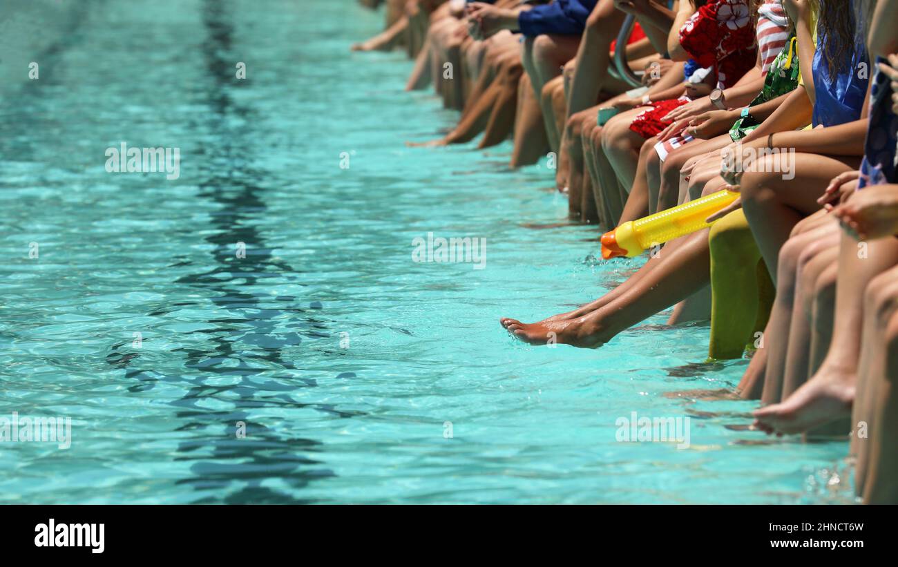 Una brillante piscina azul aqua con estudiantes sentados colgando sus pies y pies en el agua. Escuela secundaria de natación carnaval o club rac Foto de stock