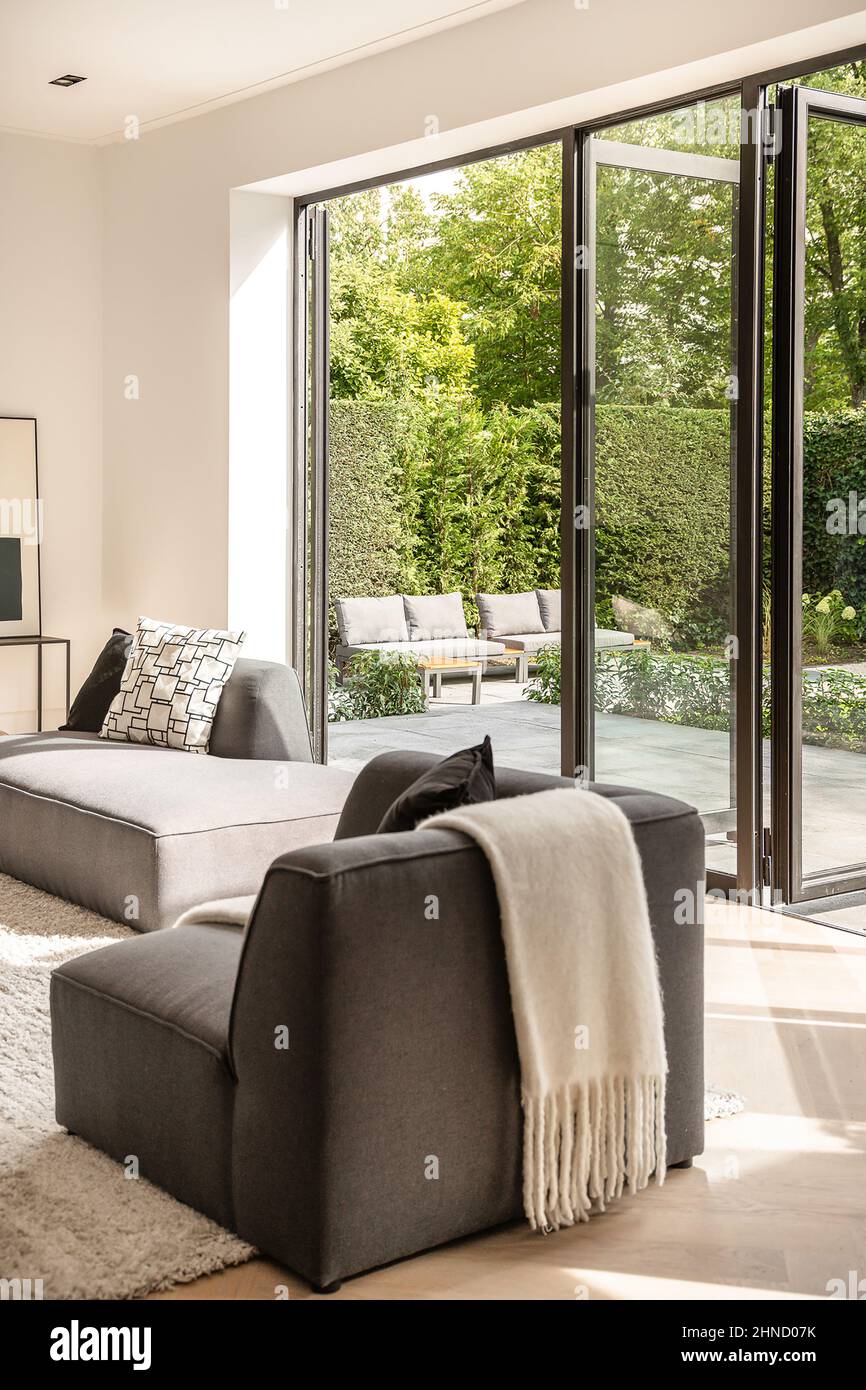 Interior de un salón moderno con muebles cómodos y cojines en la alfombra cerca puertas de vidrio abiertas trasero la villa Fotografía de stock - Alamy