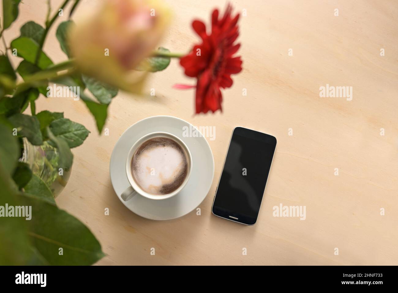 Taza de café y teléfono móvil bajo un ramo de flores en una mesa de madera clara, concepto de negocios para una accesibilidad constante, espacio de copia, vista superior desde abo Foto de stock