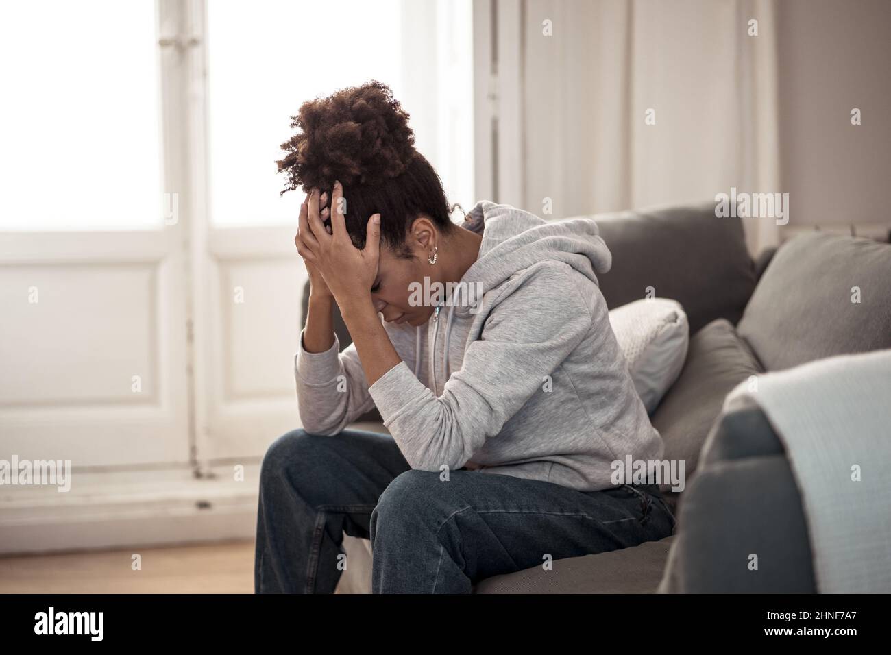 Joven atrayente afroamericana tumbada en el sofá de la sala de estar sintiéndose triste cansada y preocupada sufriendo depresión, angustia y ansiedad en mí Foto de stock