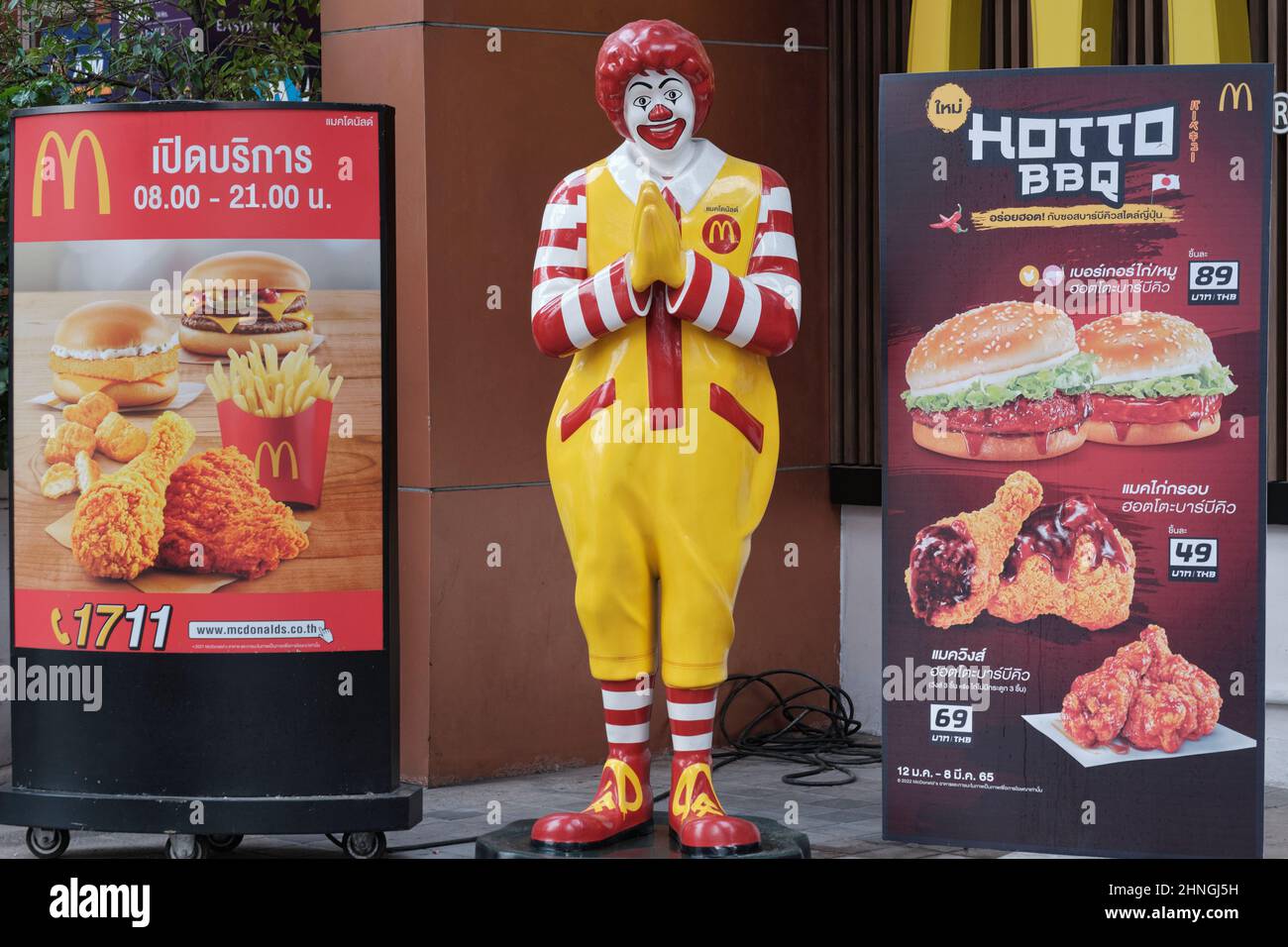 Un McDonald's outlet en Bangkok, Tailandia, el payaso de marca que representa un tradicional tailandés 'wai' (saludo) y flanqueado por pancartas de oferta especial Foto de stock