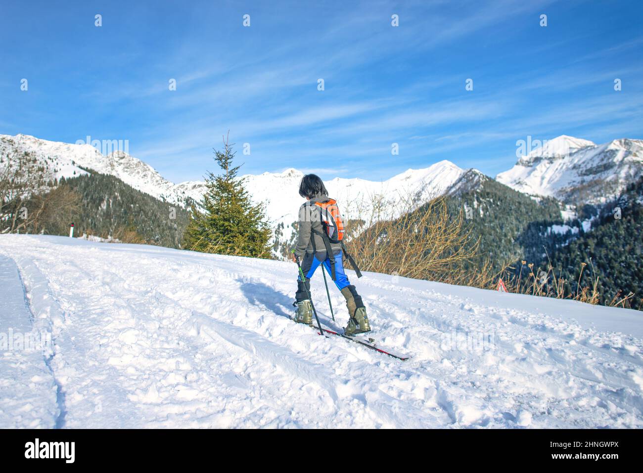 Un niño deportivo sube por la carretera nevada con esquís y pieles de mar en primavera Foto de stock