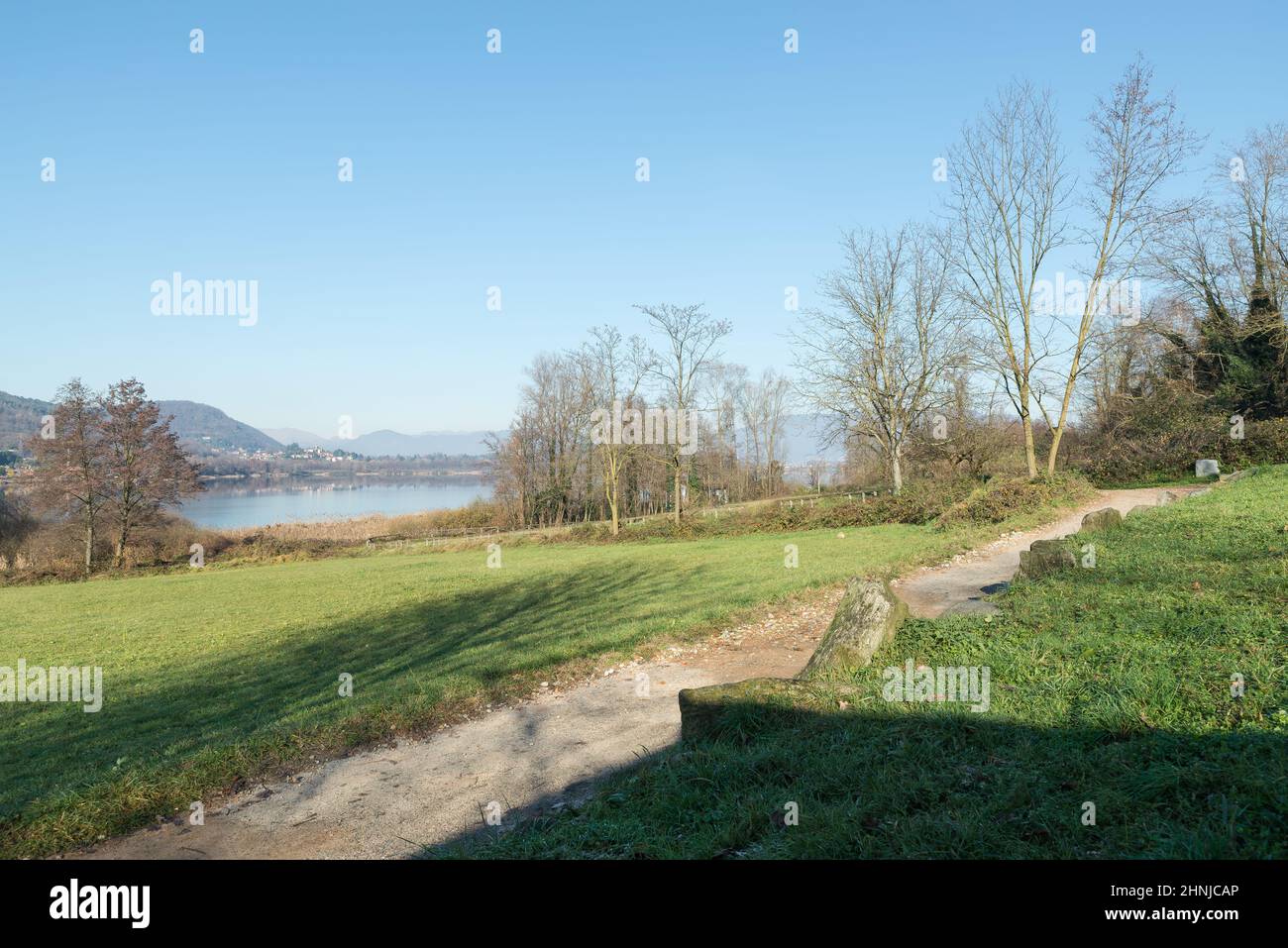 Lago con sendero para bicicletas de tierra en invierno. Lago Comabbio, al norte de Italia. En el fondo de la ciudad de Comabbio Foto de stock